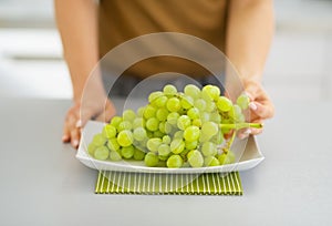 Closeup on branch of grapes on plate and woman tearing off grape