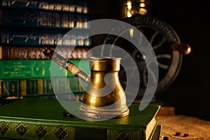 Closeup brass turk with beans beside and coffee grinder on background. Atmosphere of old library with old books around on dark