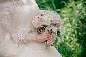 Closeup of bride hands holding beautiful wedding bouquet with white and pink roses. Concept of floristics