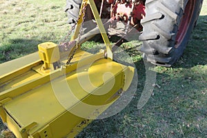 A closeup of a bright yellow slasher hooked up to a red tractor