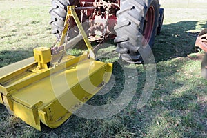 A closeup of a bright yellow slasher hooked up to a red tractor