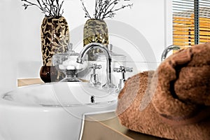 Closeup of a brown color towel and focusing modern white washstand with a faucet in luxurious house or hotel