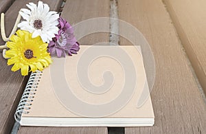 Closeup brown note book with colorful faked flower on blurred old wood table textured background