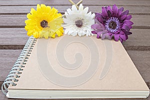 Closeup brown note book with colorful faked flower on blurred old wood table textured background