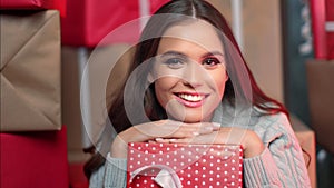 Closeup brunette female hugging red wrapped festive gift box blowing air kiss celebrating holiday