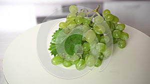 Closeup of a bunch of grapes rotating on white plate. Green grapes on kitchen table. Healthy and fresh food, good source