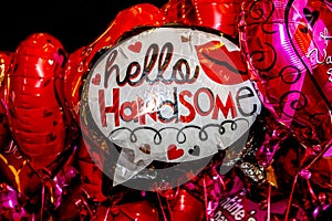 Closeup of a bunch of mylar balloons in pink and red with one in the middle that reads Hello Handsome - Selective focus
