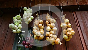 Closeup of bunch of onions Allium cepa drying on wooden background. Harvest time Hanging to dry. Pile of yellow, red onion