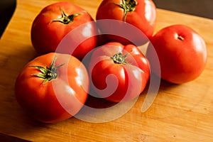 closeup of a bunch of red tomatoes on a wooden board at kitchen table