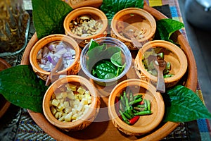 Burmese Tea Leaf Salad or Lahpet in a wooden plate with Wild Betel Leaves on a light wooden table in warm tone