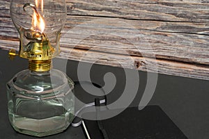 Closeup of a burning old antique hurricane oil lamp with closed book on wooden table