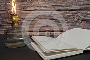 Closeup of a burning old antique hurricane oil lamp with open book on wooden table