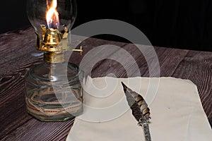 Closeup of a burning old antique hurricane oil lamp with quill pen and paper on wooden table