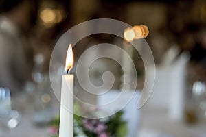 Closeup of burning white candle romantic dinner table memory memorial in front of bokeeh background photo