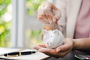 Closeup of business woman hand putting money coin into piggy bank for saving money. saving money and financial concept