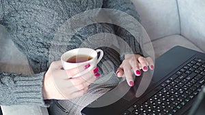 Closeup of business woman hands using touchpad on laptop keyboard and drinks tea