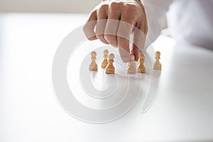 Closeup of businessman hand arranging peasant chess pieces on white office desk
