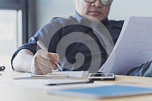 Closeup businessman hands working on finance business document reading report paperwork spreadsheet using laptop at office desk.