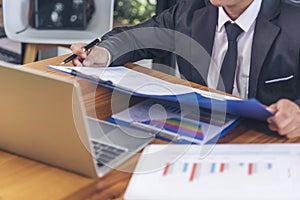 Closeup businessman hands working on finance business document reading report paperwork spreadsheet using laptop at office desk.