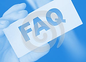 Closeup on businessman holding a card with text FAQ , business concept image with soft focus background