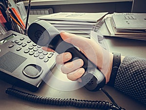 Closeup Of Businessman Holding Handset Of A Black Landline Telephone