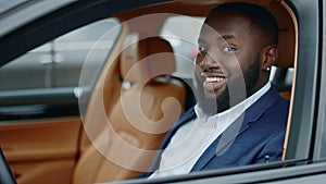 Closeup businessman looking at camera at car. African man smiling in luxury car