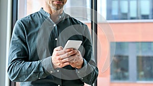 Closeup of businessman male hands holding using smartphone in office.