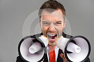 Closeup of businessman screaming in two megaphones on grey background. photo