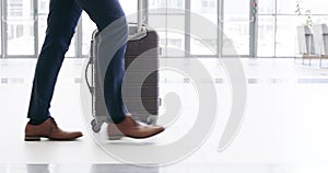 Closeup businessman in suit, legs walking through the airport to catch a plane with suitcase next to him. Traveling
