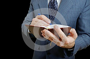 Closeup of a businessman taking notes in a small notebook.