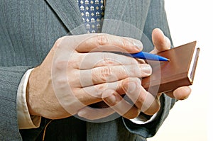 Closeup of a businessman taking notes in a small notebook.