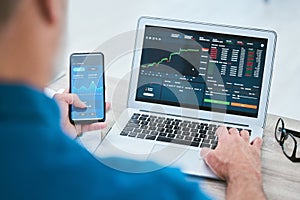 Closeup of a businessman using a phone and laptop, trading on the stock market in a financial crisis. Online trader with
