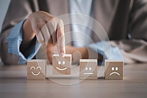 Closeup businesswoman hand picking happy emotion face on wooden cube arranged on table for satisfaction survey