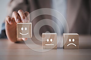 Closeup businesswoman hand picking happy emotion face on wooden cube arranged on table for satisfaction survey