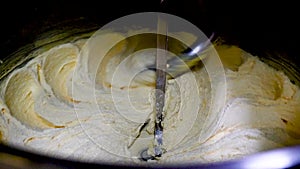 Closeup of butter being whipped in large industrial mixer