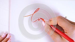 Closeup of calligrapher hands writes word LOVE on white paper. Inscribing ornamental decorated letters. Calligraphy