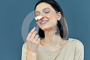 Closeup candid portrait of a gorgeous brunette young woman smiling during making makeup with a brush in hand against blue studio