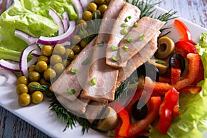 Closeup canned tuna slices with fresh vegetables on white plate top view