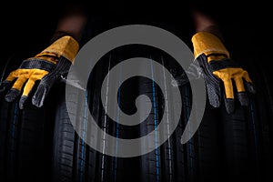 Closeup of car tires and men hands in yellow rubber gloves black background. Concept of car service.