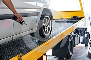 Closeup on car towed onto flatbed tow truck with cable