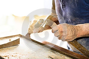 Closeup of a carpenter hands working with a chisel and hammer on wooden workbench