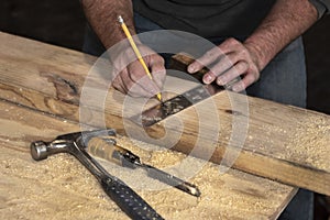 Closeup of carpenter marking line on wooded board with pencil and wooden square during home remodel