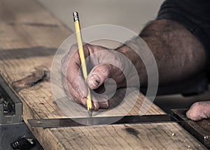 Closeup of carpenter`s rough hands using a pencil and old square to mark a line on a wooden board to saw