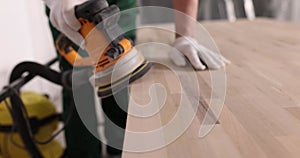 Closeup of carpenter sanding wooden table by orbital sander in workshop