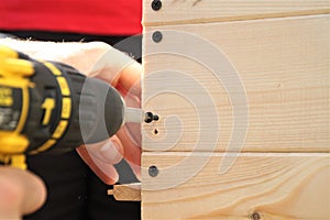 Closeup of a carpenter screwed a hinge on a wooden plank.