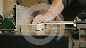 Closeup of a carpenter using a table saw to cut a plank of wood while working in his woodworking studio