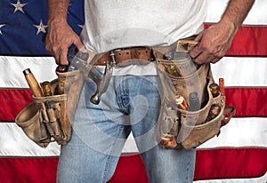 Closeup carpenter wearing old, worn out leather toolbelt in front of American flag photo