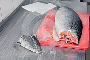 Closeup carving whole fresh norwegian salmon fish with heads on red cutting board in professional kitchen restaurant, preparing