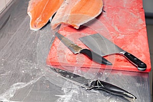 Closeup carving whole fresh norwegian salmon fish with knife on red cutting board in professional kitchen restaurant, preparing