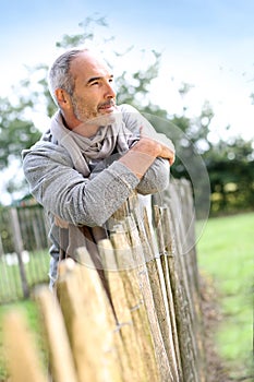 Closeup of casual senior man leaning on wood fence